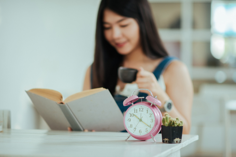Person reading a book with coffee and an alarm clock during a calm, screen-free morning
