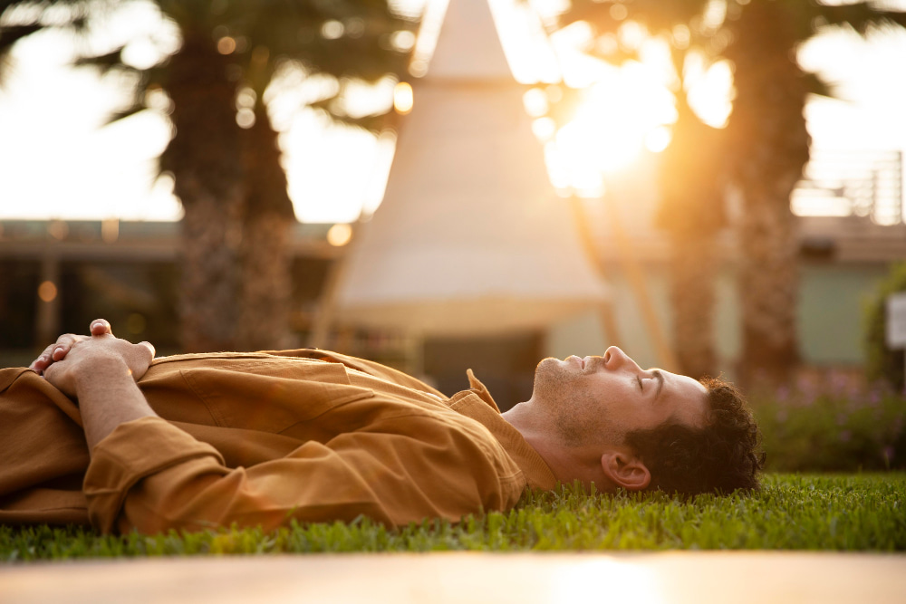 Person lying on grass with eyes closed, enjoying a slow and relaxed mindful moment
