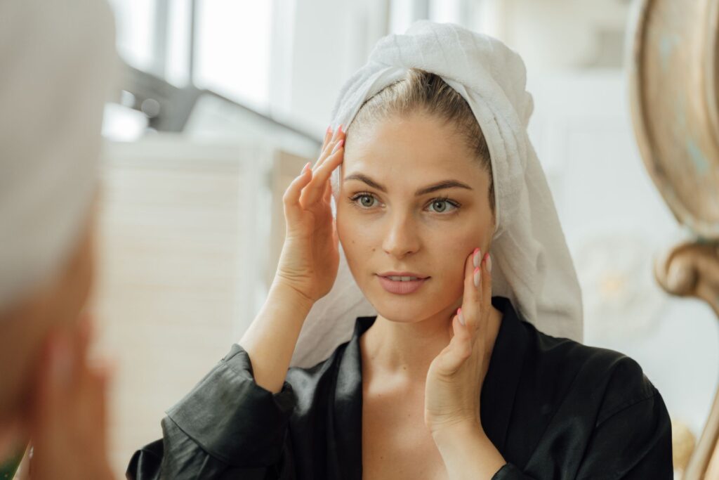 Woman checking healthy-looking skin in the mirror while following skincare tips along with neem for a balanced daily skincare routine.